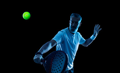 Padel tennis player with racket. Man athlete with paddle tenis racket on court with neon colors. Sport concept. Download a high quality photo for the design of a sports app or betting site. - obrazy, fototapety, plakaty