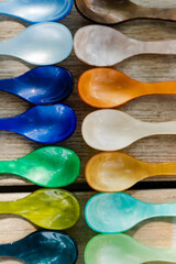 Vertical shot of two rows of colorful acrylic teaspoons laid out on wooden table outside