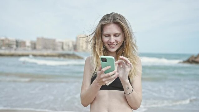 Young blonde woman tourist wearing bikini make selfie by smartphone at beach