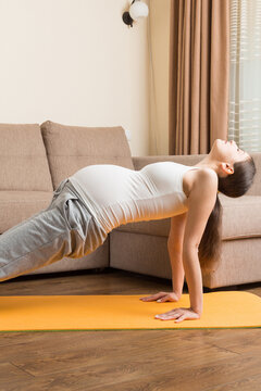 beautiful young pregnant woman sitting near sofa in yoga pose at the home. Pregnancy Yoga and Fitness concept at coronavirus time