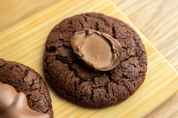 A round chocolate cookie with half of a chocolate egg lies on a wooden kitchen board