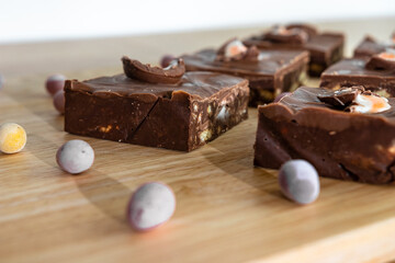 Slices of chocolate cake with chocolate eggs of various sizes are placed on a wooden table near a chef