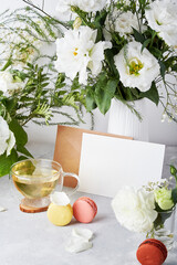 Paper envelope with stationery card mock up for greetings, invitation, text with white flowers, macarons and tea cup. Aesthetic table settings, cozy home. Copy space