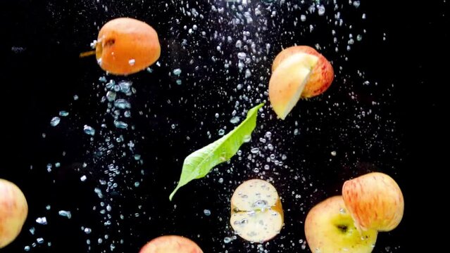 fruits splashing into the water in slow motion. Lots of apples falling slowly on a black background. Tomatoes and apples red and yellow are isolated on a black background. Fresh water with fruits.