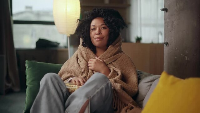 Close up portrait of happy positive young curly woman with popcorn while watching comedy movie show serial enjoying leisure time sitting on couch at home alone Fun weekend time