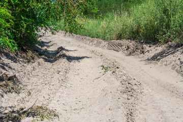 Obraz premium Sand road in the forest. Tire pattern of quad bike on driveway. Track imprint of quadricycle on nature land. Sand texture off road. Path in forest close up. Sand mounds and green forest in sunny day.