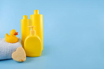 Yellow empty mock-ups of shampoo bottles, a blue towel, soap and a yellow rubber duck. Things for bathing a child.Empty space for text or logo on a blue background.