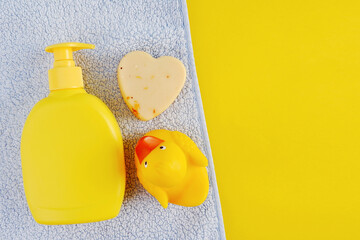 A yellow empty mock-up of a shampoo bottle, a blue towel, soap in the shape of a heart and a yellow rubber duck. Things for bathing a child.Empty space for text or logo on a yellow background.