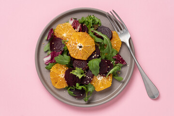 Seasonal vitamin salad orange beetroot and arugula in plate on pink background. Diet, healthy eating concept
