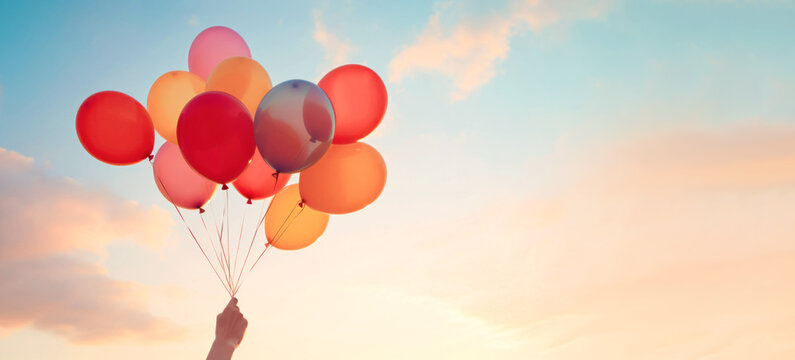 Balloons Around the World Day. Female hand with Colorful balloons on sky background. Festive balloons in air web wide banner