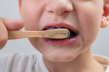 7-year-old boy without one milk tooth brushes his teeth with a bamboo brush