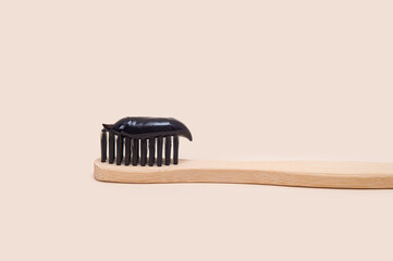 Black toothpaste on a bamboo brush with black bristles on a beige background.