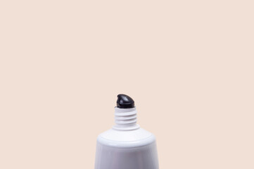 White tube with black toothpaste on a beige background.