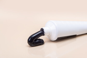 White tube with black toothpaste on a beige background.