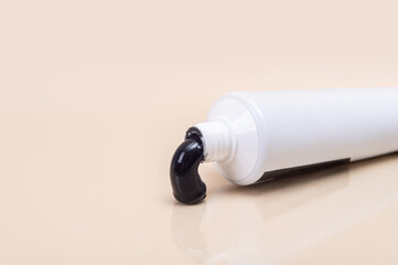 White tube with black toothpaste on a beige background.