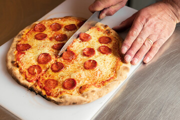 A chef cuts freshly baked pizza just out of the hot oven,