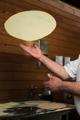 A skillful chef is preparing pizza, twirling the dough, making thin crust for delicious Italian pizza in an upscale restaurant