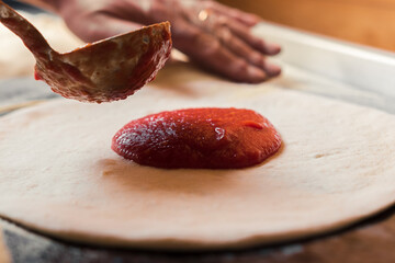 A man spreads Italian tomato paste over the dough, part of the pizza preparation process at the family café