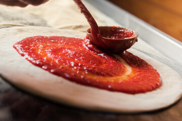 A man spreads Italian tomato paste over the dough, part of the pizza preparation process at the family café