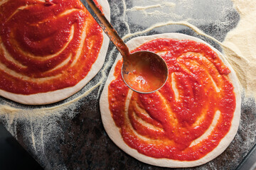 A woman adds tomato paste to the dough, preparing pizza for baking in a restaurant
