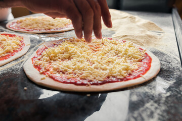 An Italian chef adds and spreads cheese over dough with tomato paste