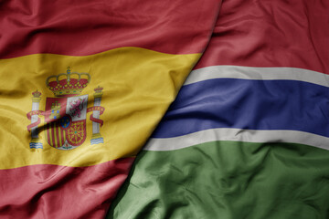 big waving national colorful flag of spain and national flag of gambia .