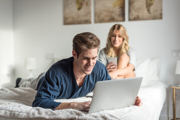 couple on bed entertained on their computer and phone