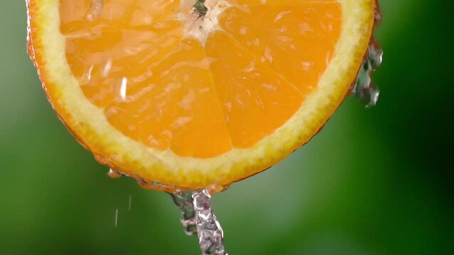 Super slow motion shot of sliced orange slice with splashes of water flying in air on green background. Freshness and refreshing invigorating citrus. Lemonade or juice Slow motion. Drops.