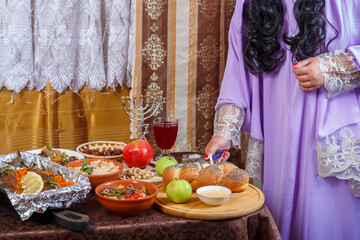 A woman's hand lights candles at a set table on the Jewish holiday Rosh Hashanah before a meal.