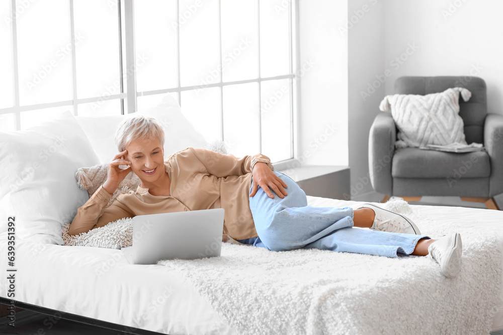 Poster Mature woman with laptop lying in bedroom