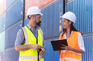 Asian dock control man and woman logistics worker wear safety helmets and protect suite working in shipping container, commercial transport background.