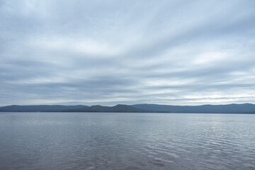 Dense gray thunderstorm cumulus clouds and a lake, water with waves. A gloomy rainy day at sea with beautiful clouds
