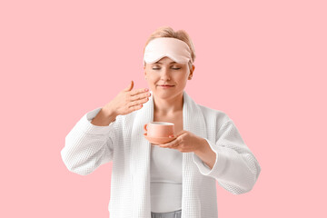 Young woman in sleeping mask with cup of coffee on pink background