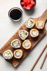 Tasty sushi rolls, soy sauce and ginger on light background