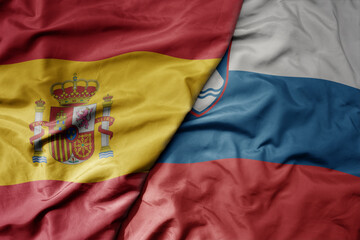 big waving national colorful flag of spain and national flag of slovenia .