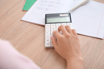 Woman working with calculator on wooden table, closeup