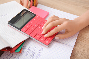 Woman working with calculator on wooden table, closeup