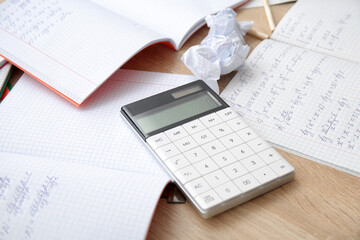 Calculator and copybooks with math formulas on wooden table