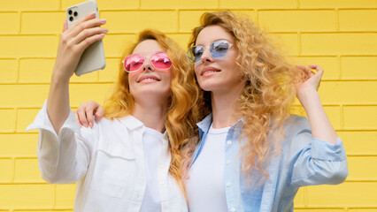 Selfie, friends, and woman posing with phone outside, peace sign for social media post. Two women sister, fashionable with mobile smartphone friendly smiling, taking cool profile picture on yellow