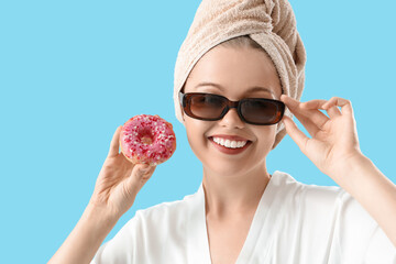 Cool young woman after shower and with donut on blue background