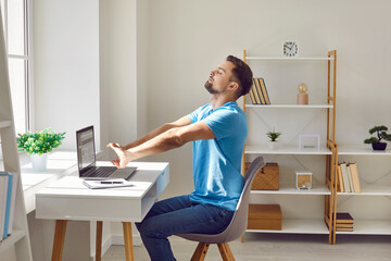 Relaxed tired young business man resting in office finishing his job well done. Male employee stretching arms relaxing at the desk on comfort chair with closed eyes on his workplace.