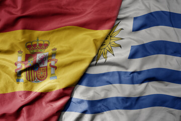 Fototapeta premium big waving national colorful flag of spain and national flag of uruguay .