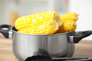 Cooking pot with boiled corn cobs on wooden table in kitchen