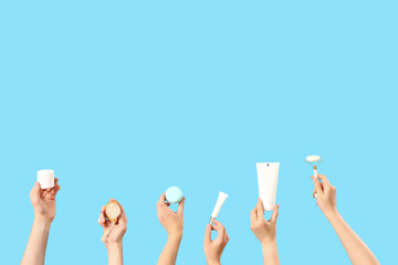 Female hands holding different cosmetic products on blue background