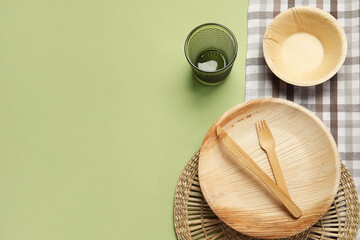 Wooden plate, bowl, cutlery and glass on green background