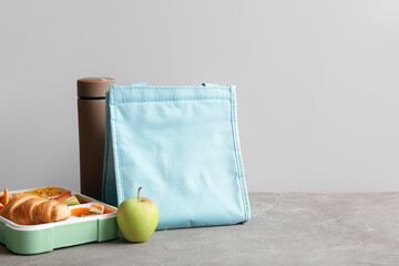 Bag, lunchbox with delicious food and thermos on grunge grey table near wall