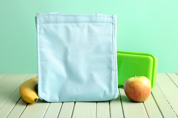 Bag, lunchbox with delicious food and fruits on green wooden table near wall