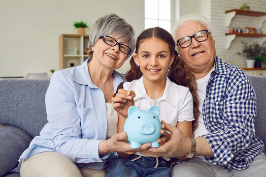 Happy family helps child save up money in piggy bank. Grandchild learns basics of financial literacy from grandparents. Smiling grandma, grandpa and girl sitting on sofa with family piggybank moneybox