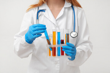 Female lab worker holding test tubes with colorful samples in stand on white background