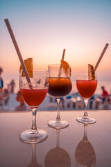 Colorful drinks in bar with blur beach party people and colorful sunset sea sky in background....